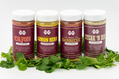 11 oz jars of barbeque, cajun and lemon herb seasonsing and 14.5 oz jar of steak and rib seasoning surrounded by cilantro